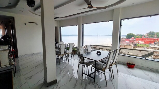 Un área de comedor con mesa y sillas, ventanas amplias con vista a un cuerpo de agua y un puente, y un ventilador de techo.