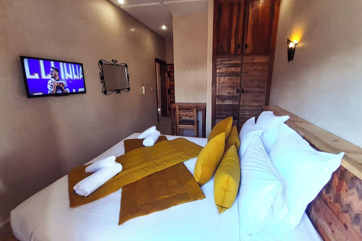 A neatly made bed with towels and pillows, a television on the wall, and a wooden wardrobe.