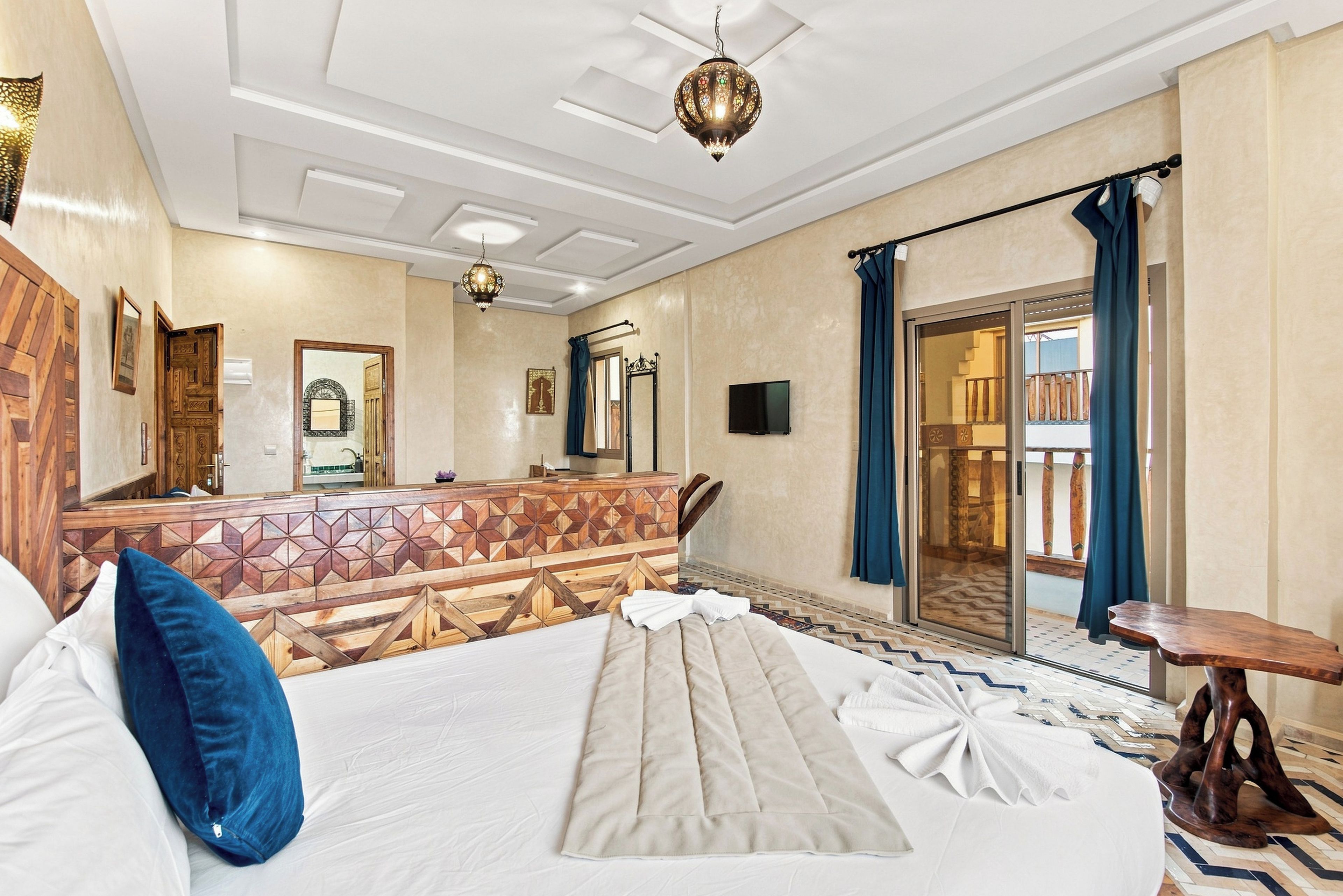 A hotel room with a bed, a wooden headboard, a television, and a balcony with a view.