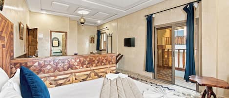 A hotel room with a bed, a wooden headboard, a television, and a balcony with a view.