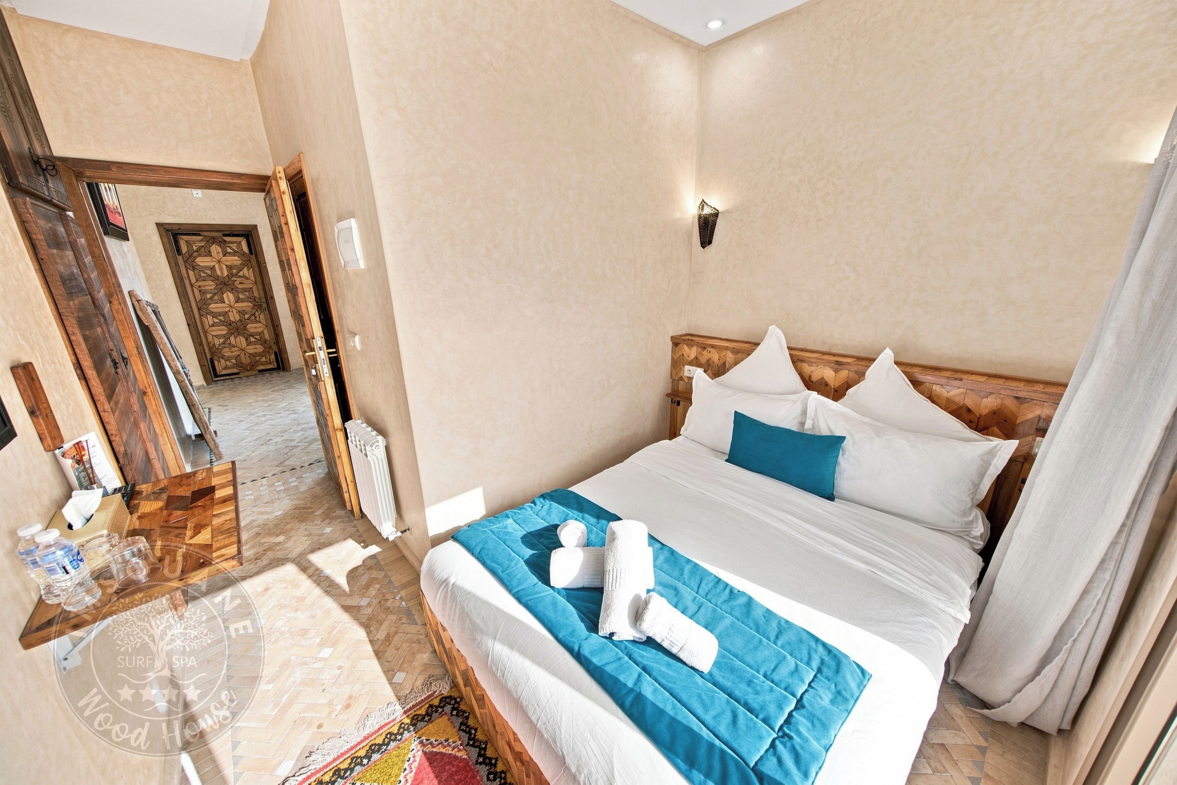 Una habitación de hotel con una cama, cabecera de madera, mesita de noche, espejo y una puerta.