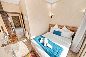 Una habitación de hotel con una cama, cabecera de madera, mesita de noche, espejo y una puerta.