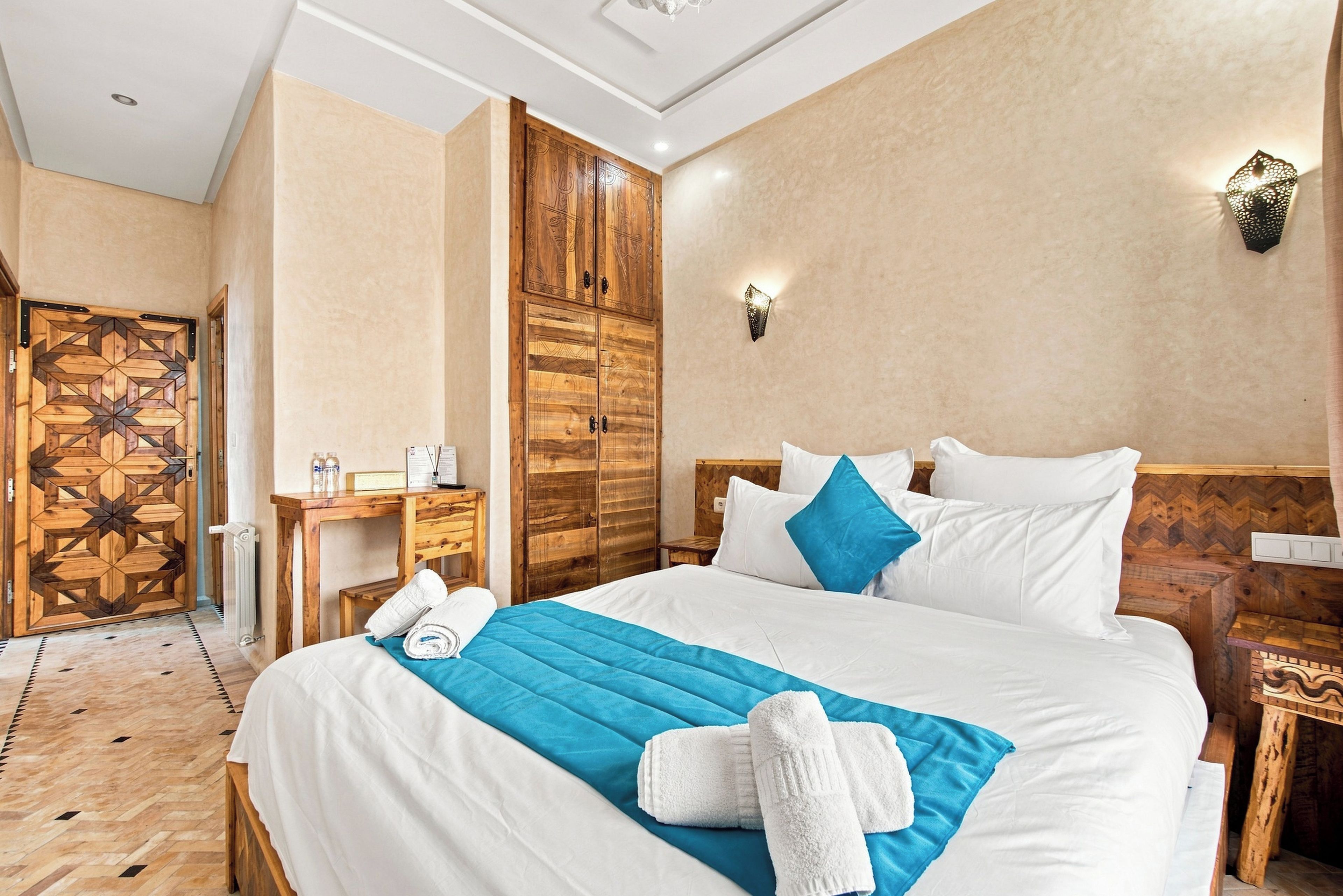 A hotel room with a bed, bedside tables, a wooden wardrobe, and a wall-mounted light fixture.