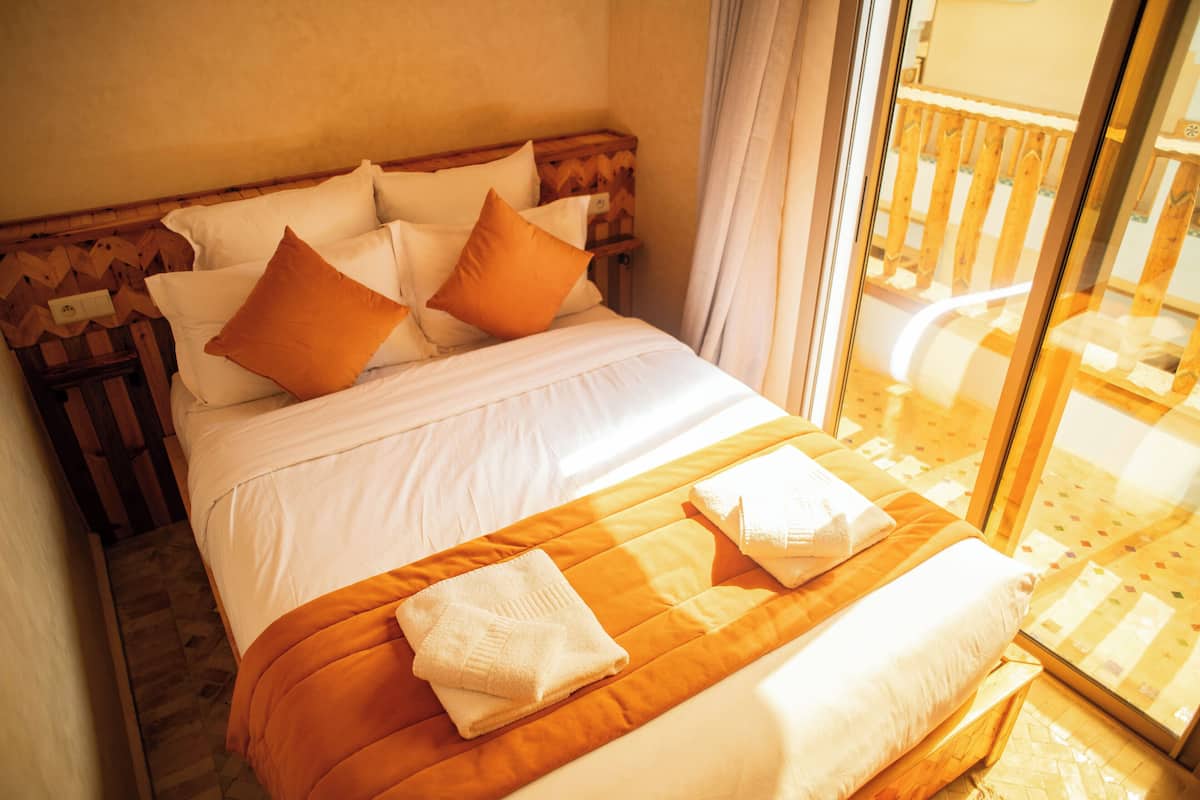 A hotel room with a large bed, wooden headboard, and a view of a balcony.
