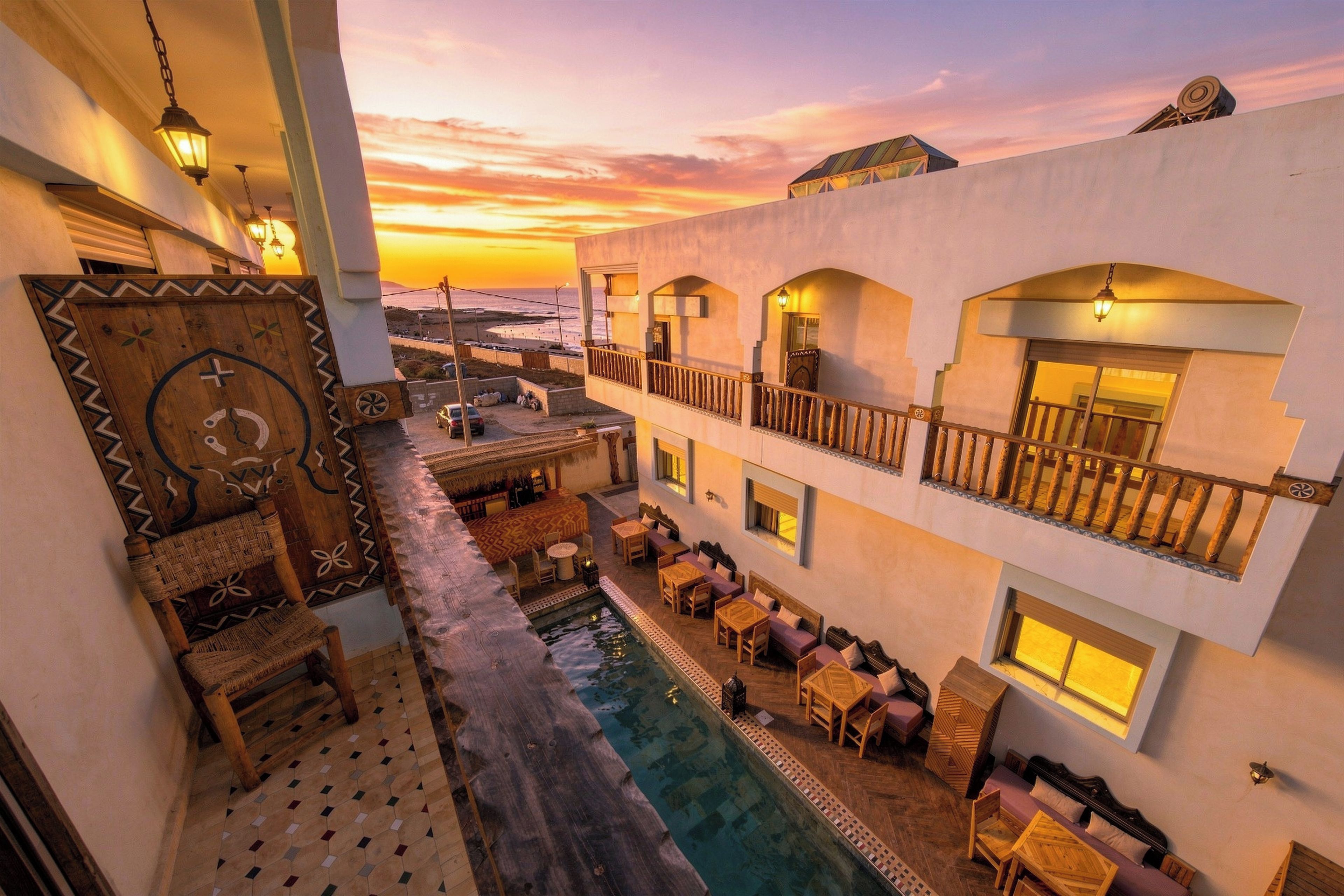 A hotel with a pool, outdoor seating, and a view of the beach at sunset.