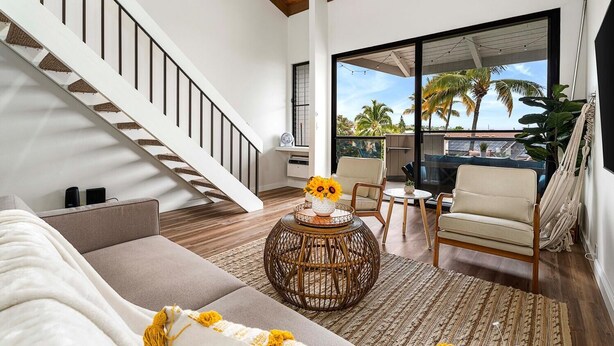 Una sala de estar moderna con una escalera, un ventanal con vistas a palmeras y una hamaca.