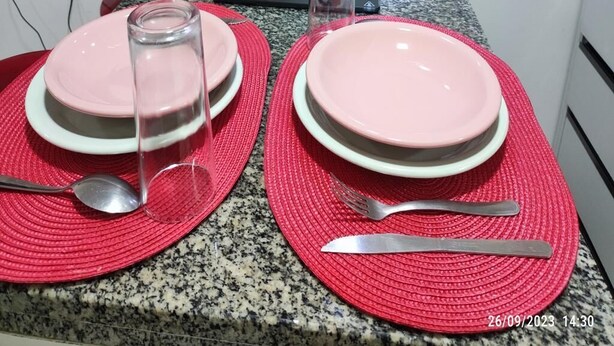 Una barra de cuina amb dos plats rosos, un bocal de vidre, una cullera i un ganivet sobre fundals vermells.