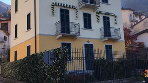 A multi-story building with balconies, a stone wall, and a paved street. - Emi s House (Lezzeno)