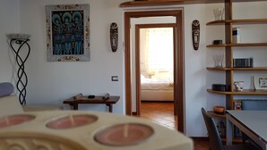A room with a bed, a table with a white tablecloth, a shelf with books, and a painting on the wall. - Emi s House (Lezzeno)