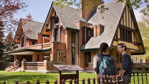 Perinteinen talo, jossa on suuri ja huomiota herättävä kuisti, kiviverhous ja jyrkkä katto.