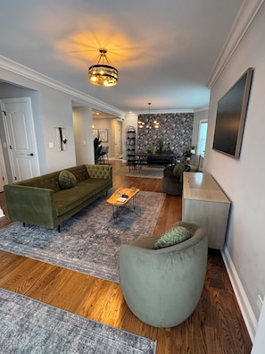 A modern living room with a sofa, armchair, coffee table, and a dining area with a chandelier. - Space&style New rehab, first flr + bsmt of duplex, driveway prkng, walk to train (Oak Park)