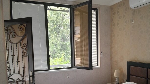 Une chambre à coucher avec un lit, une fenêtre avec des stores, une porte dotée d’une poignée décorative et un appareil de climatisation fixé au mur.