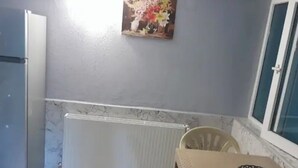 Une cuisine de taille réduite comprenant un réfrigérateur, un radiateur, une table à manger avec des chaises et une fenêtre donnant sur un paysage agréable.