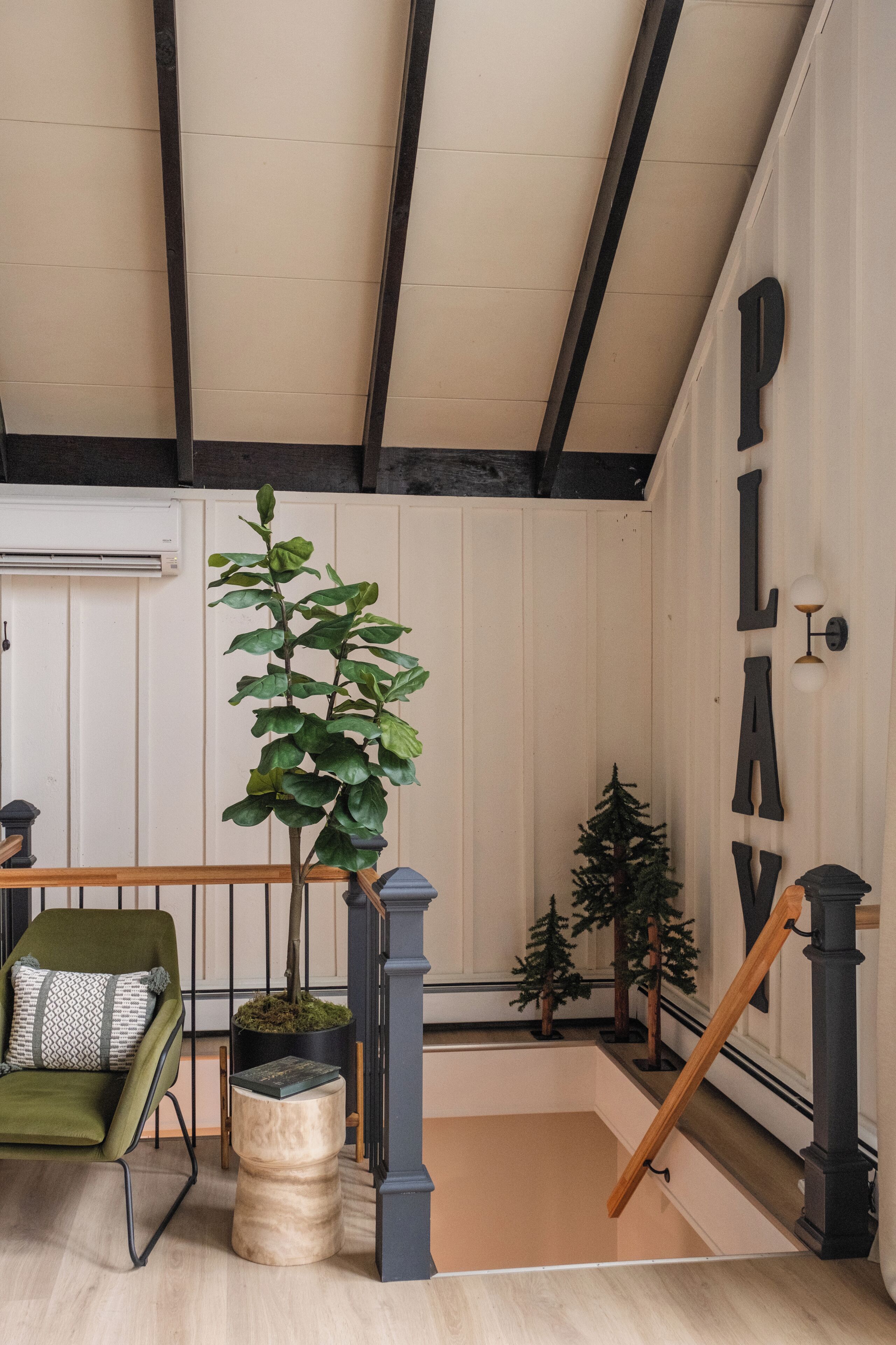 Una escalera con barandilla de madera y balaustrada negra, una silla verde con cojines estampados y una planta en maceta.