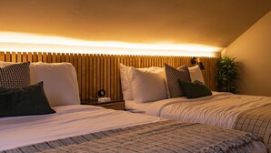 Habitación de hotel con dos camas, cabecero de madera y mesita de noche con lámpara.