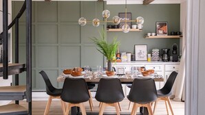 Comedor con mesa dispuesta para cuatro, sillas negras, un centro de mesa con planta y una estación de café al fondo.