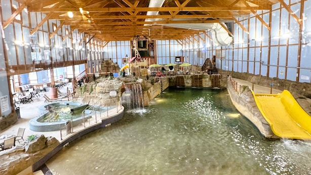 Ein Indoor-Wasserpark mit zentralem Pool, Wasserrutschen und einer Holzbalkendecke.