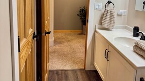 A bathroom with a wooden door, a sink, a mirror, and a towel rack. - Charming woodland villa located in a secured resort across from Starved Rock  (North Utica)