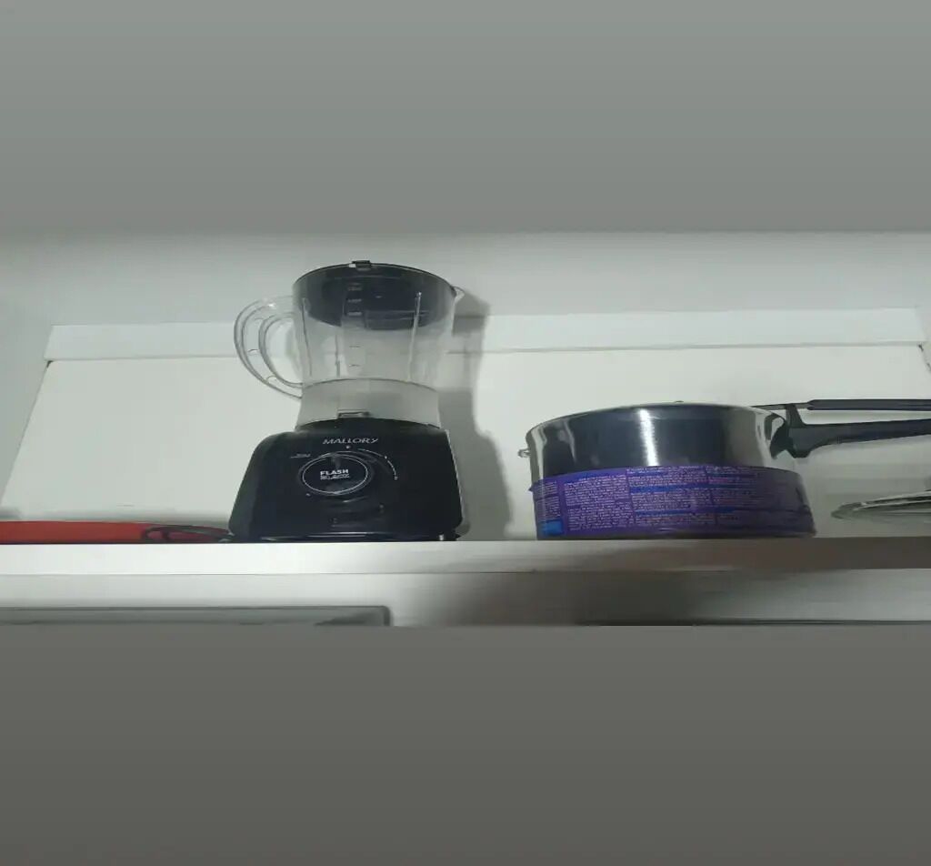 Uma cozinha com um liquidificador, uma panela e um recipiente vermelho na bancada.