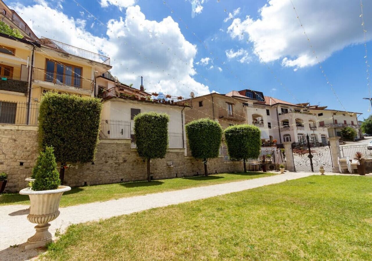 A courtyard with a pathway, neatly trimmed hedges, and a stone wall.