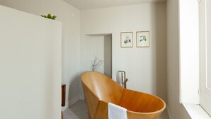 Ein modernes Badezimmer mit einer freistehenden Holzbadewanne, weißen Wänden und zwei gerahmten Pflanzenbildern.