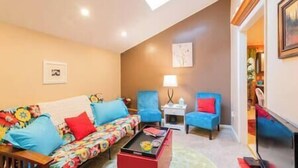 Un salon comprenant un canapé, une table basse et deux fauteuils. Un tableau est accroché au mur et une lampe se trouve sur une table d’appoint.