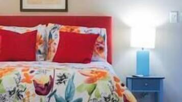 A bedroom with a bed, red pillows, a floral bedspread, a nightstand with a lamp, and a framed picture on the wall.