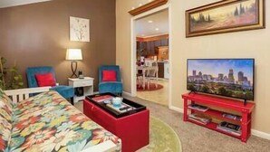 Un salon avec un canapé, une table basse, un téléviseur posé sur un meuble et un tableau accroché au mur.