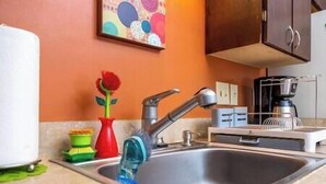 Une cuisine avec un évier en acier inoxydable, un vase rouge contenant une fleur et une machine à café.