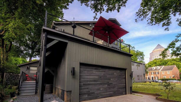 Un bâtiment moderne doté d’une grande porte de garage, d’un escalier menant à un balcon et d’un parasol rouge sur le toit.