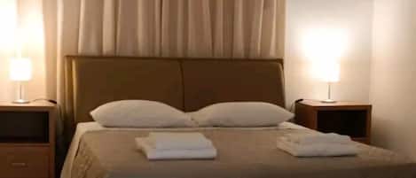 A bedroom with a bed, two bedside tables, a ceiling fan, and sheer curtains.