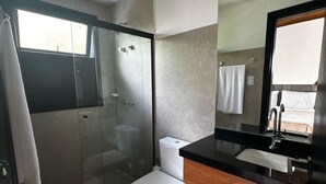 A modern bathroom with a glass-enclosed shower, a white toilet, and a wooden vanity with a mirror.