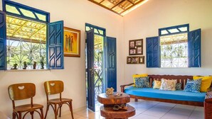 A room with a blue sofa, two wooden chairs, a round wooden table, and a large window with blue shutters.