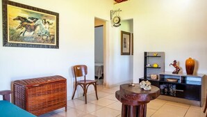 A room with a wooden cabinet, a chair, a small round table, and a painting of horses on the wall.