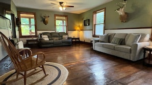 A spacious living room with hardwood floors, two sofas, a rocking chair, and a ceiling fan.