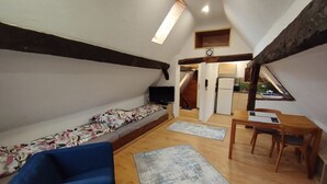 A loft-style room with a bed, a blue sofa, a dining table with chairs, and a small kitchen area. - Open loft apartment / parking space (Alsfeld)