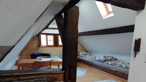 A loft-style bedroom with a sloped ceiling, wooden beams, a bed, a desk, and a window. - Open loft apartment / parking space (Alsfeld)