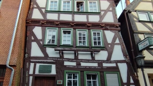 A traditional half-timbered building with a prominent wooden door and multiple windows with green shutters. - Open loft apartment / parking space (Alsfeld)