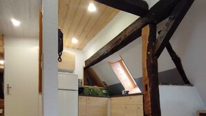 A loft-style room with exposed wooden beams, a kitchenette, and a sloped ceiling. - Open loft apartment / parking space (Alsfeld)