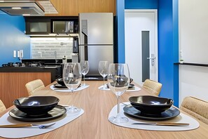 A modern kitchen with a microwave, refrigerator, and stove. There is a dining table set with black bowls, wine glasses, and cutlery. - HomyCO - Conforto na esqui praia (Niteroi)
