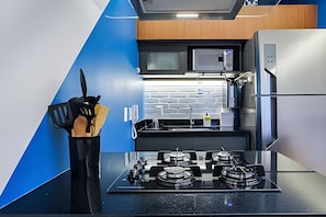 A modern kitchen with a black countertop, stainless steel appliances, and a blue accent wall. - HomyCO - Conforto na esqui praia (Niteroi)