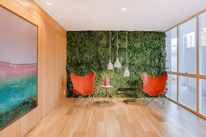 Un espacio de oficina moderno con una pared verde, dos sillas rojas, una mesa pequeña y lámparas colgantes.
