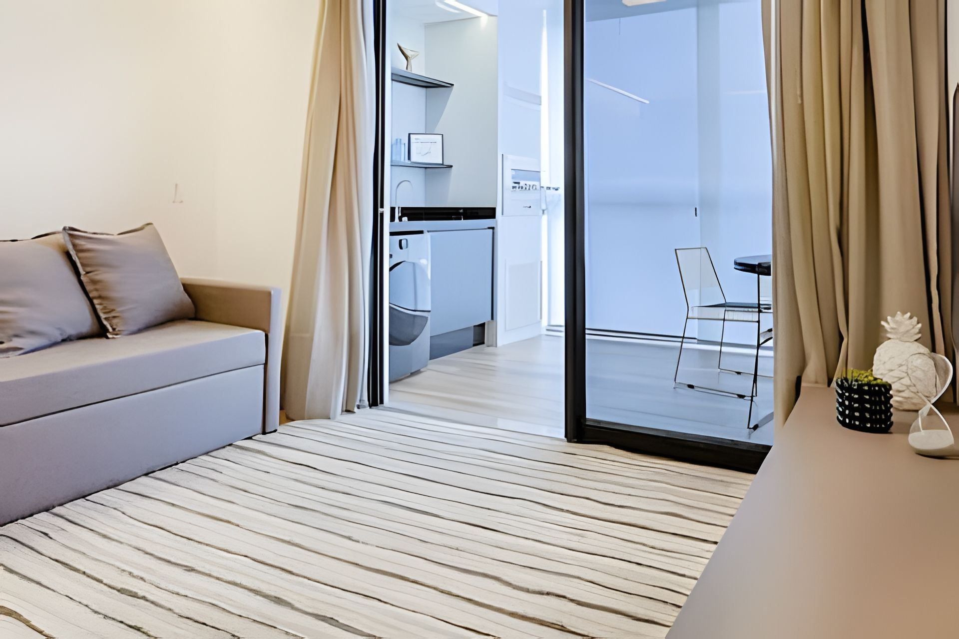 A modern living room with a sofa, a dining area with a table and chairs, and a kitchen visible through an open door.