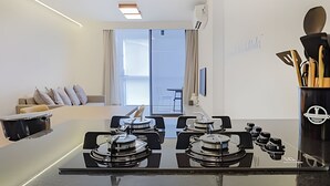 A modern kitchen with a gas stove, a dining area with a sofa and a table, and a view of the outside through a large window. - HomyCO - Conforto na esqui praia (Niteroi)
