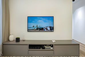 A wall-mounted TV on a grey entertainment unit with a remote control, a small decorative pineapple, and a lamp. - HomyCO - Conforto na esqui praia (Niteroi)