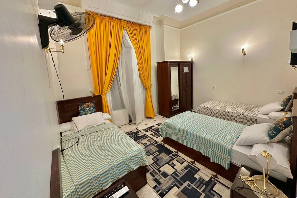 Habitación de hotel con dos camas, un armario, un espejo, un ventilador y una lámpara en el techo.