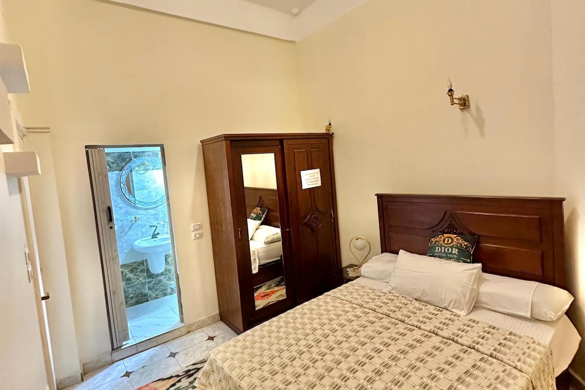 Habitación de hotel con cama, armario, baño con lavamanos y espejo, y una mesita de noche.