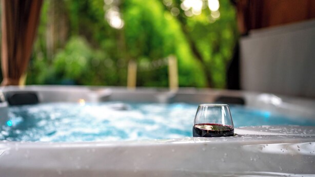 A hot tub with a glass of red wine, surrounded by a lush green outdoor setting.