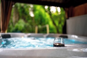 Een hottub met een glas rode wijn, omgeven door een weelderige groene buitenomgeving.