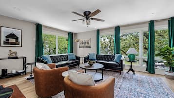 Un salon spacieux doté d’un ventilateur de plafond, de deux canapés, d’une table basse et d’une grande fenêtre avec des rideaux.
